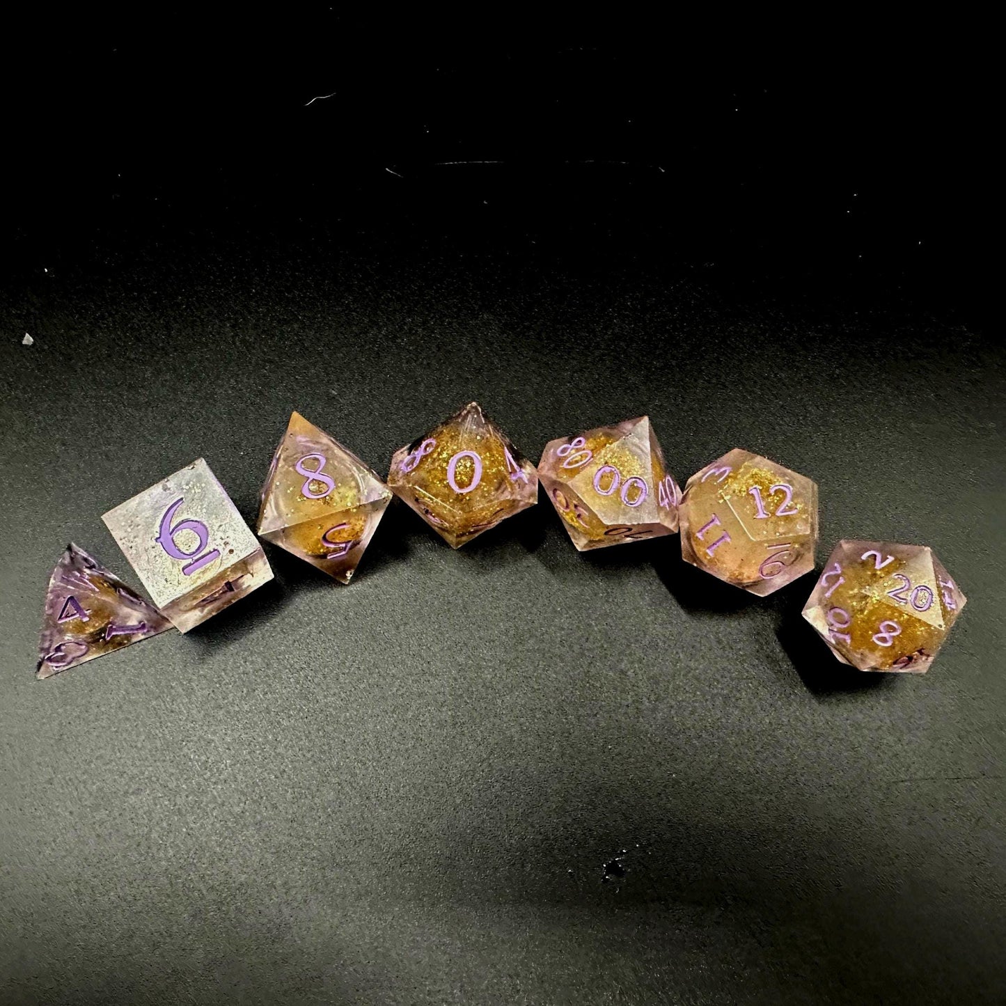 Light purple, pink, and gold glitter liquid core dice set shimmering with swirling metallic sparkle. Handcrafted polyhedral resin dice filled with floating glitter and vibrant liquid core for mesmerizing movement. Perfect for Dungeons & Dragons, tabletop RPGs, and dice collectors. Elegant pastel tones with gold accents add a magical, fantasy-inspired aesthetic for gaming sessions or gift giving.