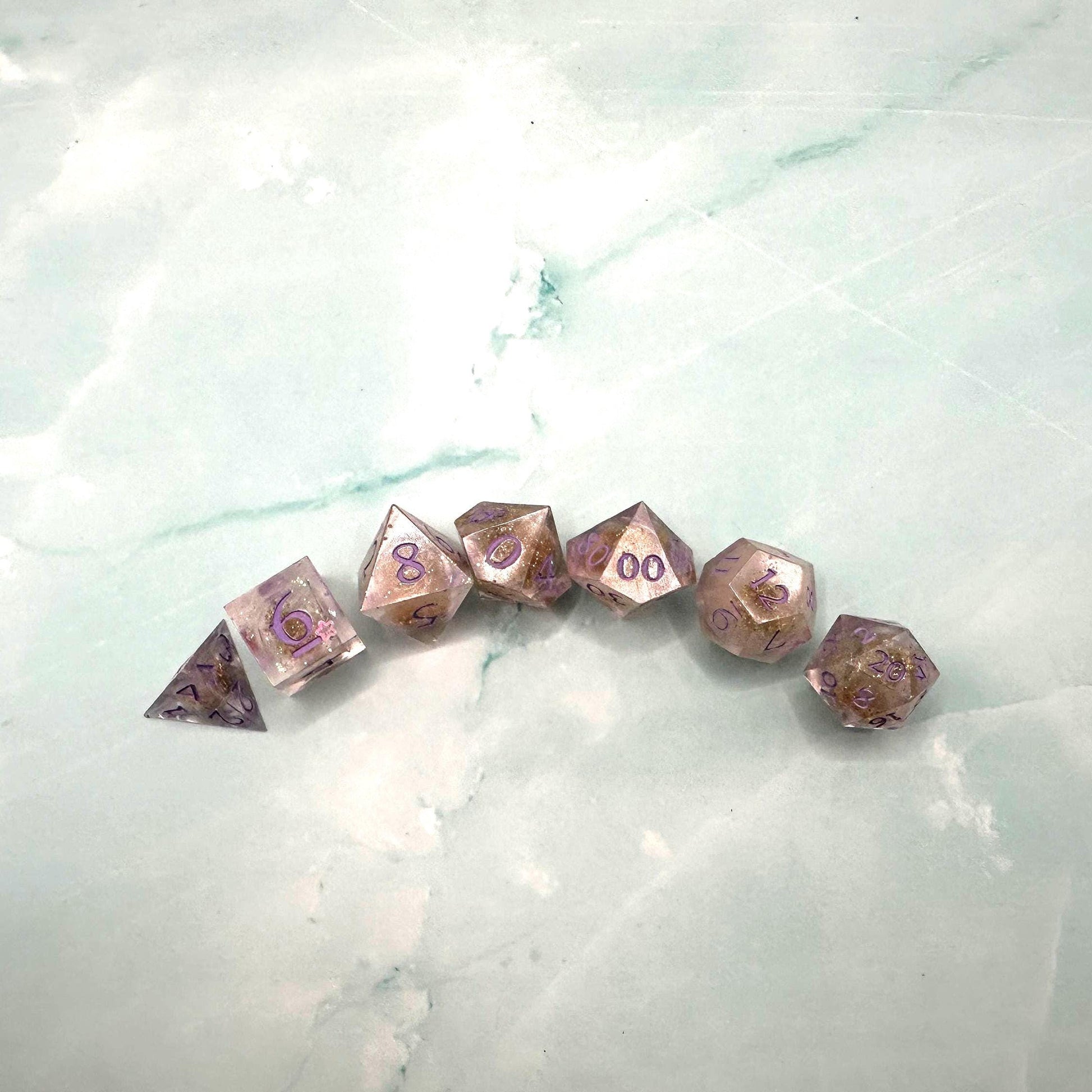 Light purple, pink, and gold glitter liquid core dice set shimmering with swirling metallic sparkle. Handcrafted polyhedral resin dice filled with floating glitter and vibrant liquid core for mesmerizing movement. Perfect for Dungeons & Dragons, tabletop RPGs, and dice collectors. Elegant pastel tones with gold accents add a magical, fantasy-inspired aesthetic for gaming sessions or gift giving.