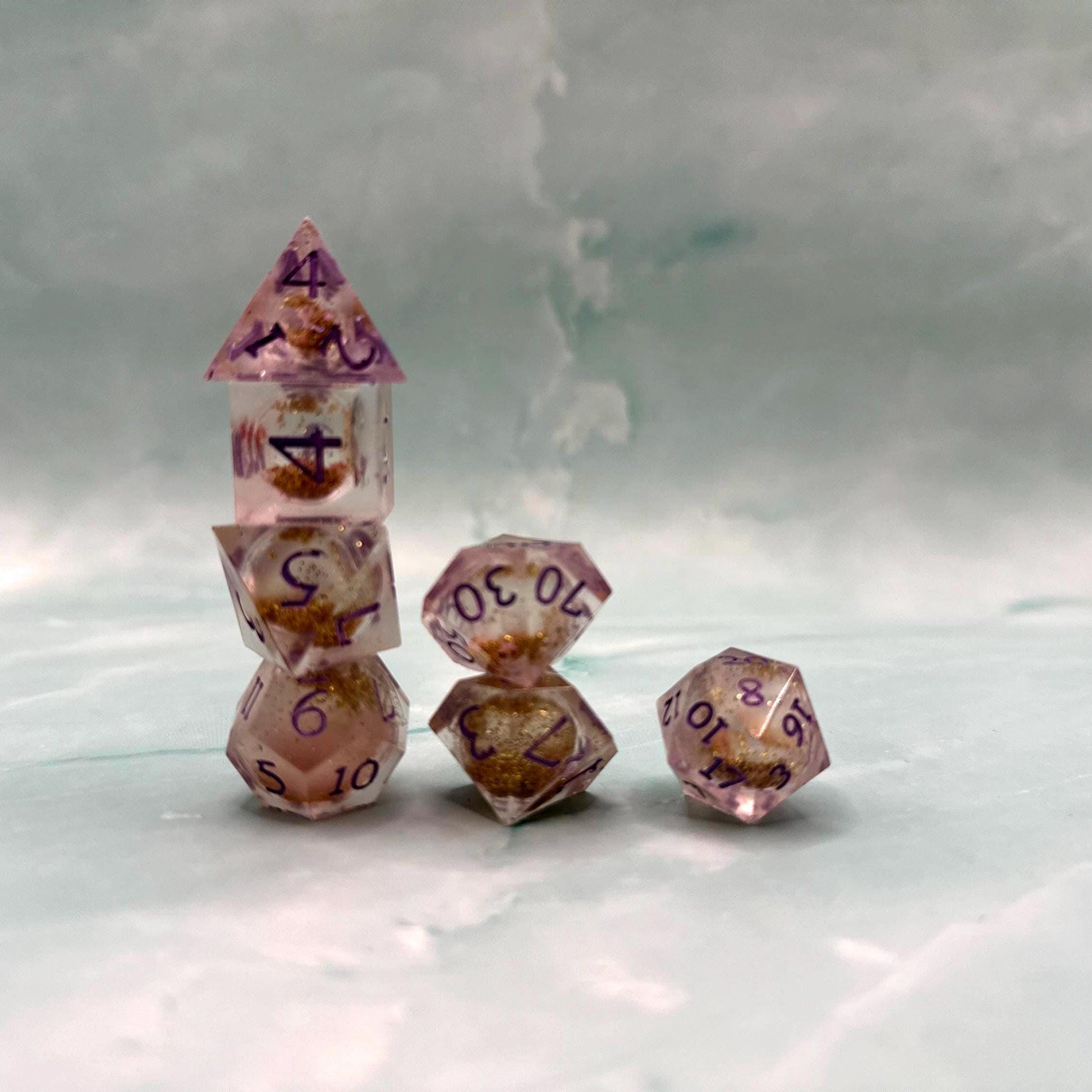 Light purple, pink, and gold glitter liquid core dice set shimmering with swirling metallic sparkle. Handcrafted polyhedral resin dice filled with floating glitter and vibrant liquid core for mesmerizing movement. Perfect for Dungeons & Dragons, tabletop RPGs, and dice collectors. Elegant pastel tones with gold accents add a magical, fantasy-inspired aesthetic for gaming sessions or gift giving.