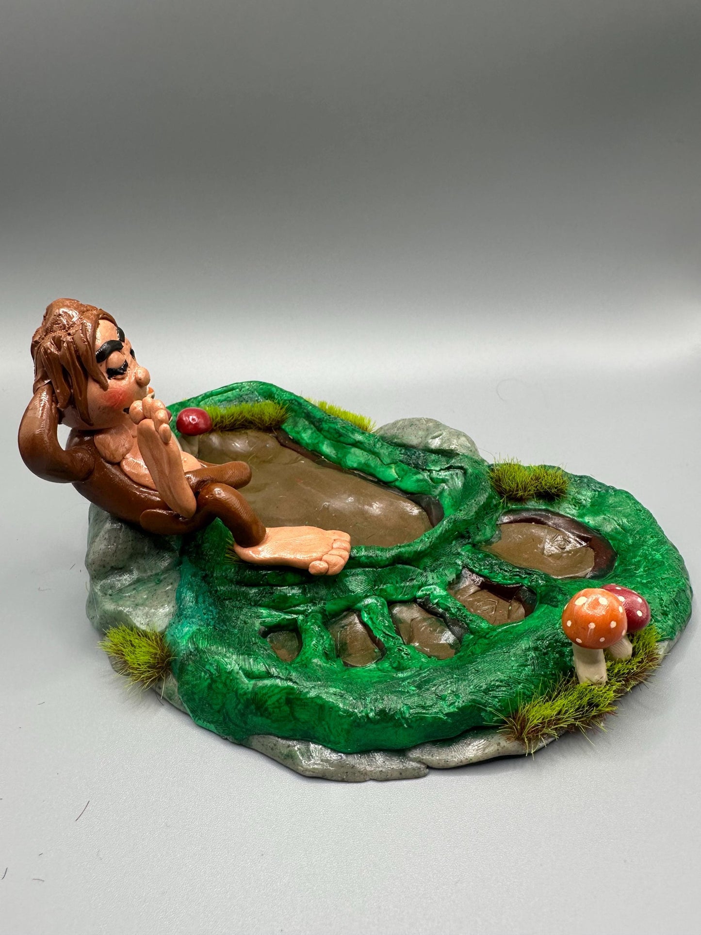 Cute handmade polymer clay dice tray and holder for a cryptid lover with a baby Bigfoot theme. Perfect gift for RPG, D&D, cryptid lovers and fantasy lovers. Baby Bigfoot sitting at the edge of a full grown Bigfoot foot print in the woods surrounded by fake grass and clay mushrooms. No AI used in the making of this dice tray!
