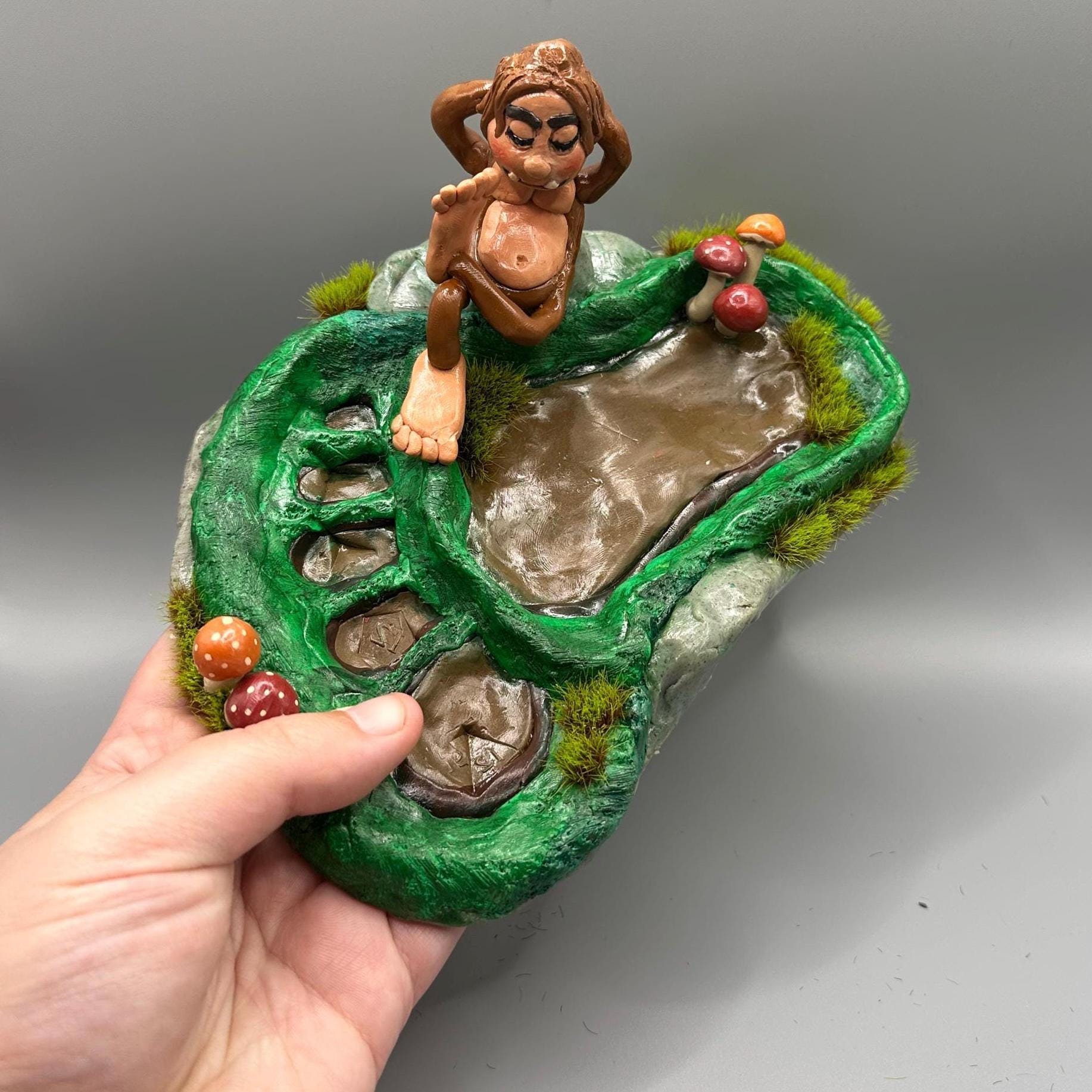 Cute handmade polymer clay dice tray and holder for a cryptid lover with a baby Bigfoot theme. Perfect gift for RPG, D&D, cryptid lovers and fantasy lovers. Baby Bigfoot sitting at the edge of a full grown Bigfoot foot print in the woods surrounded by fake grass and clay mushrooms. No AI used in the making of this dice tray!