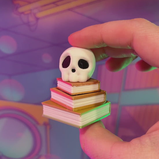 3D printed skull fidget clicker on an ombre stack of books.