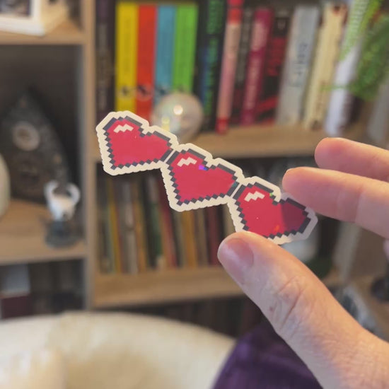 Holographic gamer heart sticker featuring 3 red pixel hearts in a heart container design. Perfect for laptops, water bottles, and game-themed journals.