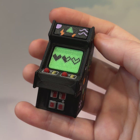 Mini retro arcade machine fidget clicker keychain with colorful 90s-inspired graphics, green screen, and 3D printed design, available in clicky or silent.