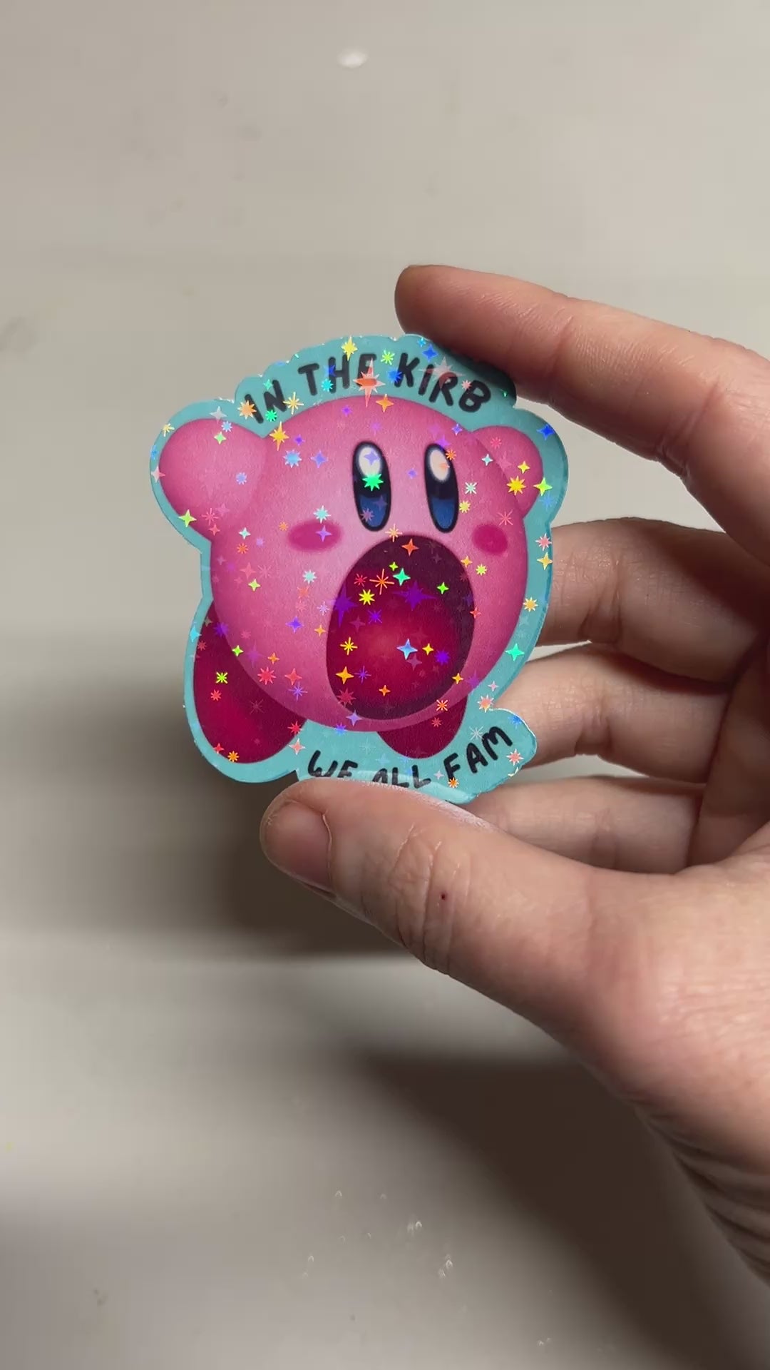 Holographic vinyl sticker featuring a cute Kirby with the phrase "In the Kirb, We All Fam." Perfect for laptops, water bottles, or gamer gear.