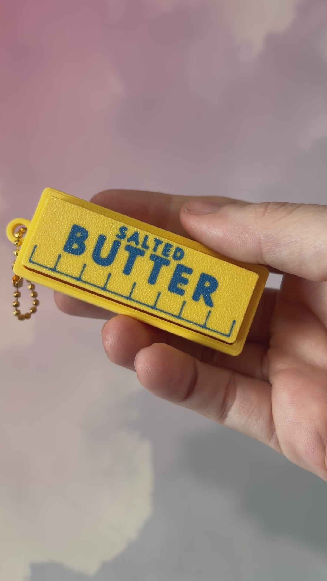 3D printed stick of butter fidget clicker keychain with classic tablespoon marking lines, gold-tone hardware, and two satisfying clicky key switches, perfect for foodies and whimsical accessory lovers.