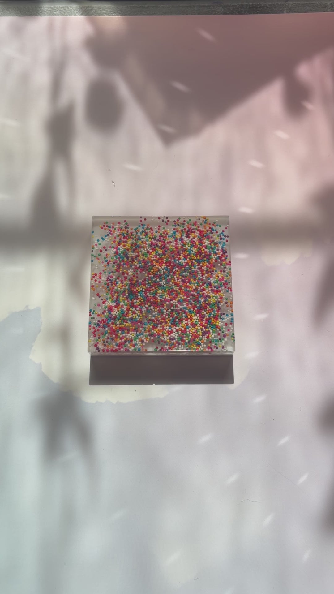 Resin coaster inlaid with rainbow sprinkles and white backing.