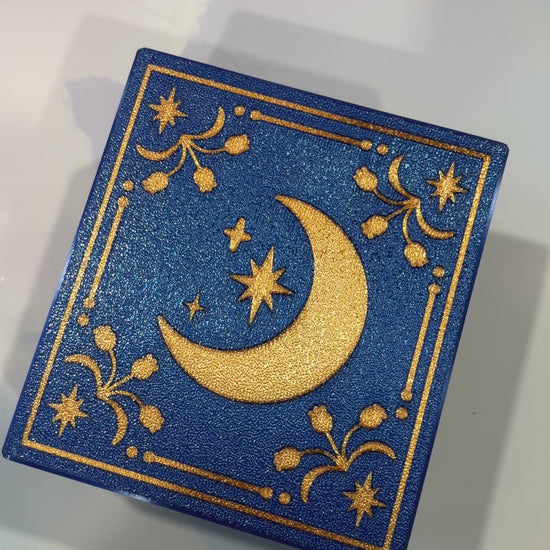 Royal blue and metallic gold 3D printed book box with a celestial moon and stars design on the cover. Opens to reveal a hidden storage compartment that holds 1–2 sets of RPG dice and doubles as a rolling tray. Perfect for jewelry, trinkets, and tabletop gaming accessories.