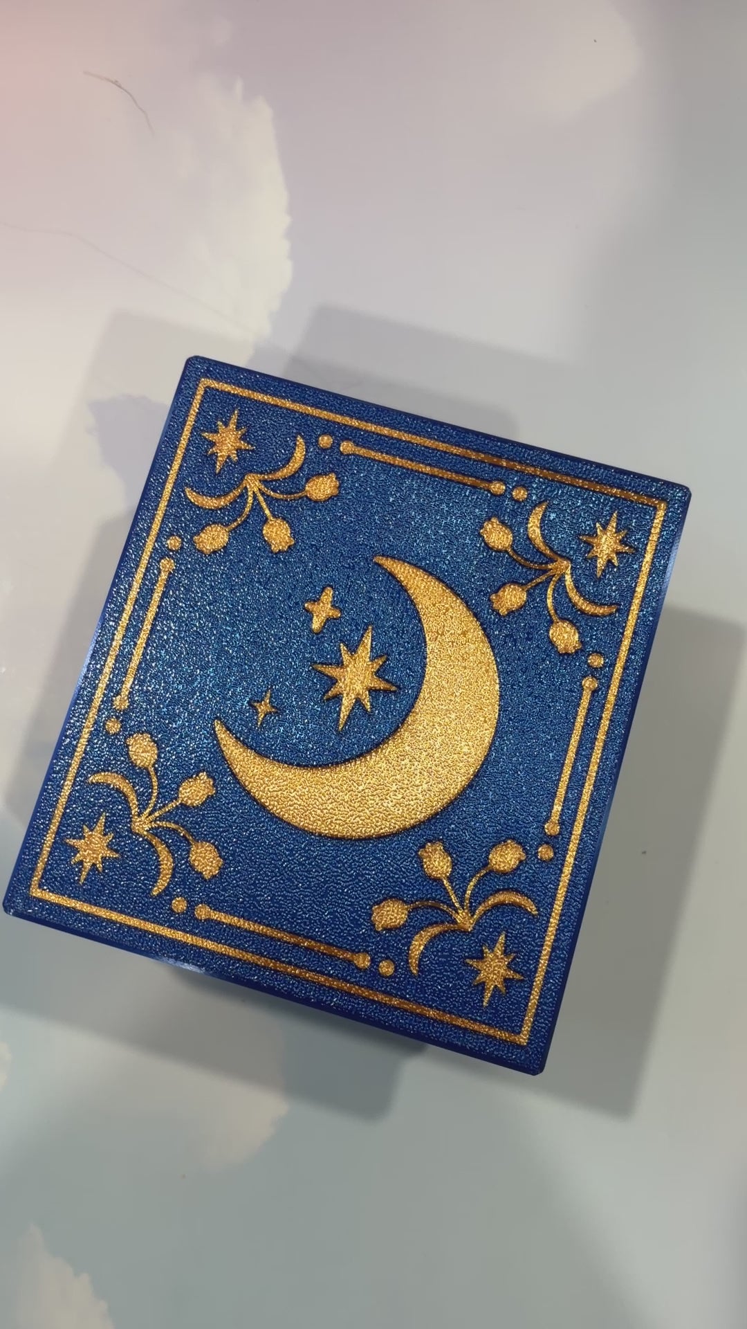 Royal blue and metallic gold 3D printed book box with a celestial moon and stars design on the cover. Opens to reveal a hidden storage compartment that holds 1–2 sets of RPG dice and doubles as a rolling tray. Perfect for jewelry, trinkets, and tabletop gaming accessories.