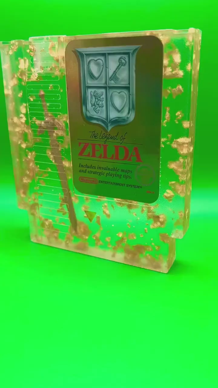 Legend of Zelda resin art featuring a retro NES cartridge with a gold sword design and gold flakes embedded. This handmade display is perfect for gamers and video game collectors, offering a unique décor piece for any gaming setup or retro collection