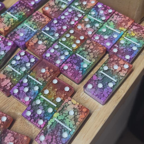 Handmade resin domino set with vibrant rainbow petri designs and holographic glitter backing. Bold black base adds contrast for striking game night flair.