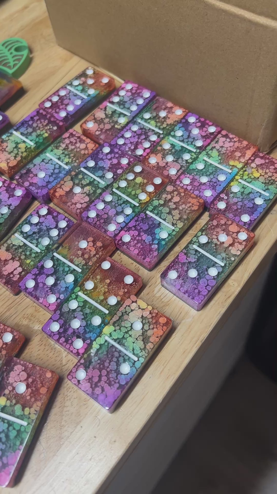 Handmade resin domino set with vibrant rainbow petri designs and holographic glitter backing. Bold black base adds contrast for striking game night flair.