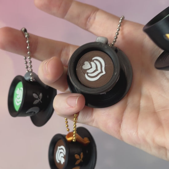 3D printed mystical drink cup fidget clicker keychain with a black floral moon design in gold or silver. Choose matcha or coffee with cute latte art, plus a clicky or silent mechanism.