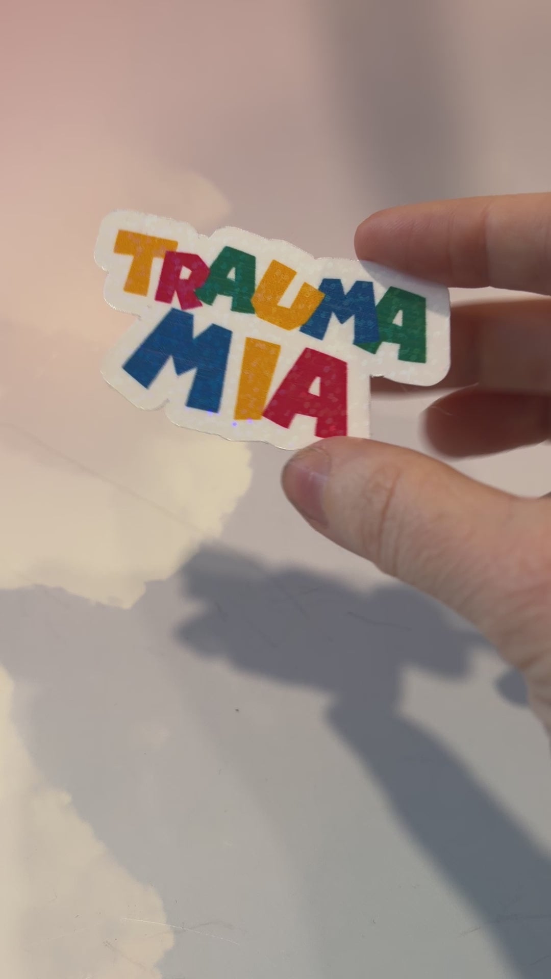 Holographic Trauma Mia sticker in retro video game style lettering.