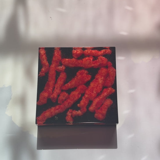 Resin coaster inlaid with Hot Cheetos and black backing.