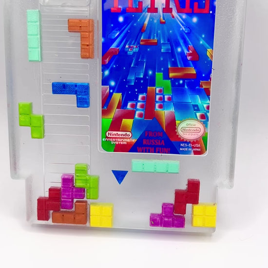 Clear resin NES cartridge art featuring vibrant 3D Tetris block embellishments for a unique retro gaming display. This handmade decorative item is a must-have for gaming enthusiasts and collectors of Nintendo memorabilia.