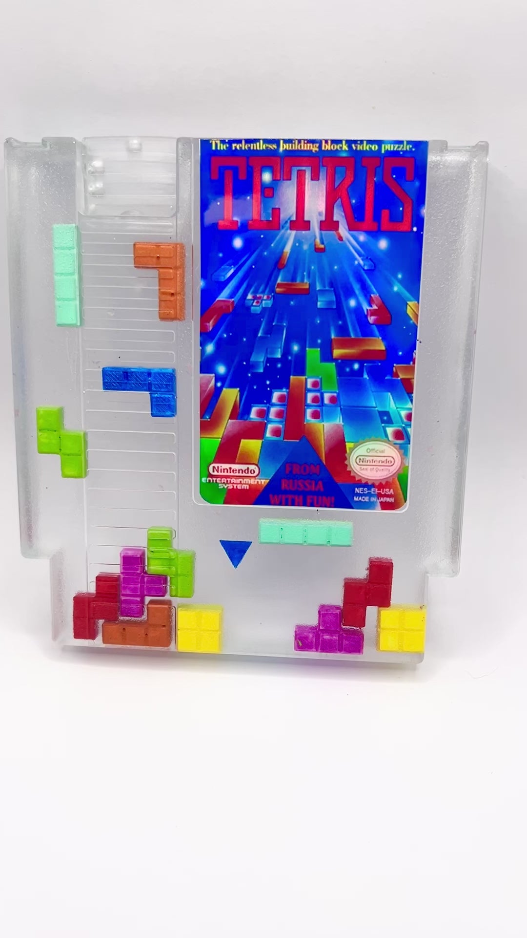 Clear resin NES cartridge art featuring vibrant 3D Tetris block embellishments for a unique retro gaming display. This handmade decorative item is a must-have for gaming enthusiasts and collectors of Nintendo memorabilia.