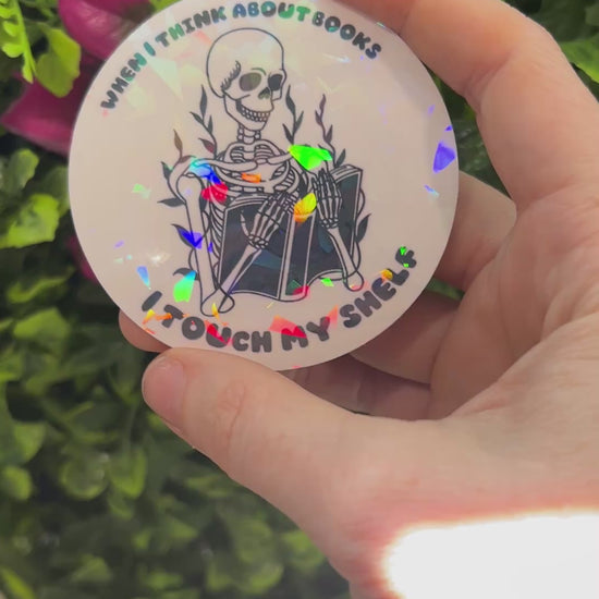 Holographic vinyl sticker with a skeleton reading a book and the phrase "When I think about books I touch my shelf." Perfect for readers and book lovers.