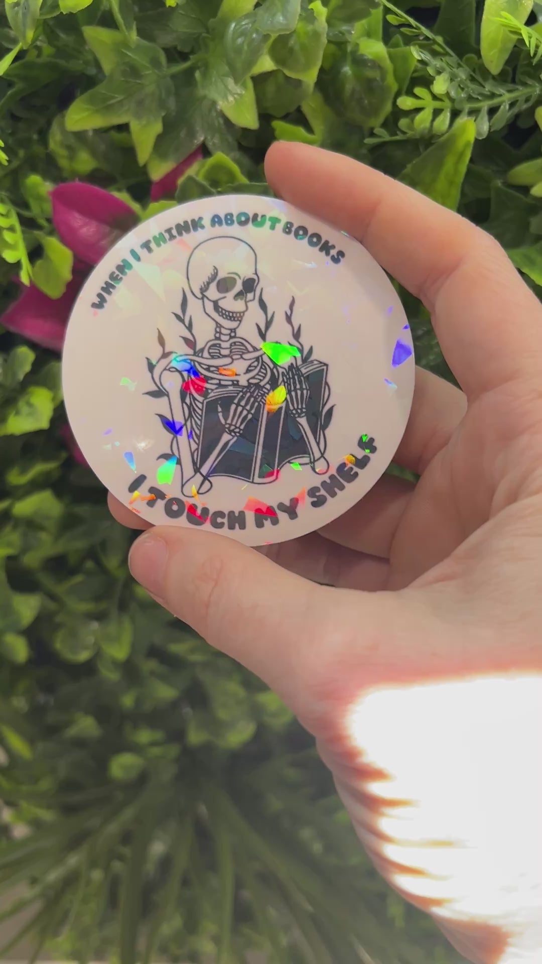 Holographic vinyl sticker with a skeleton reading a book and the phrase "When I think about books I touch my shelf." Perfect for readers and book lovers.