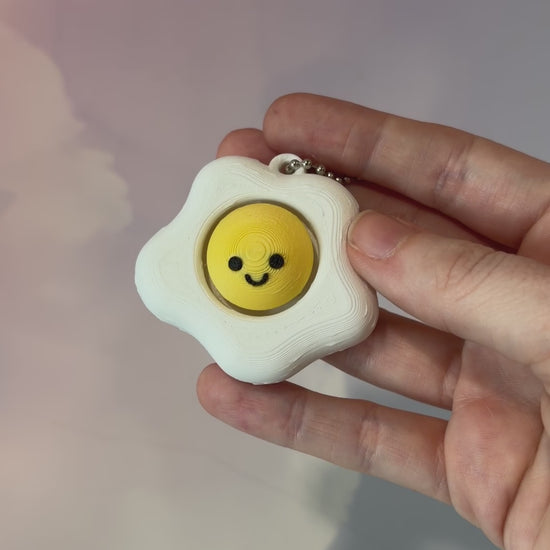 Fried egg shaped fidget clicker toy with a white egg and yellow yolk design, fun food themed desk accessory and satisfying fidget gift.