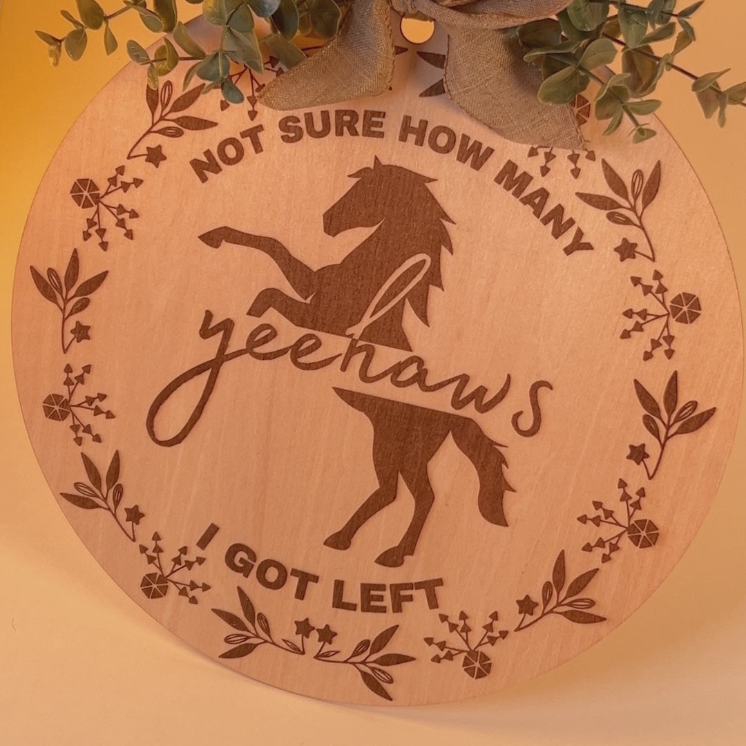 Laser-engraved wood sign featuring 'Not Sure How Many Yeehaws I Got Left,' decorated with a horse silhouette, floral accents, and a rustic bow.