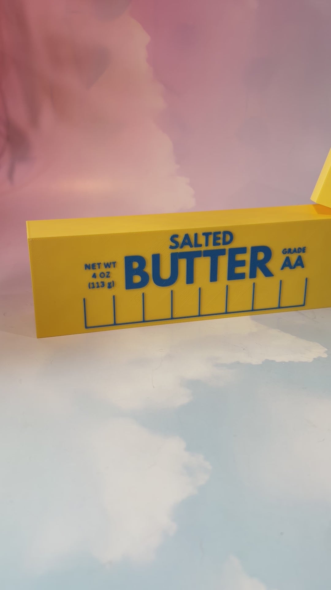 Oversized 3D printed novelty stick of butter, approximately 8.5 inches long, featuring classic tablespoon measurement lines, Grade AA labeling, and net weight details. Whimsical food-themed decor for kitchens and farmhouse-style homes.