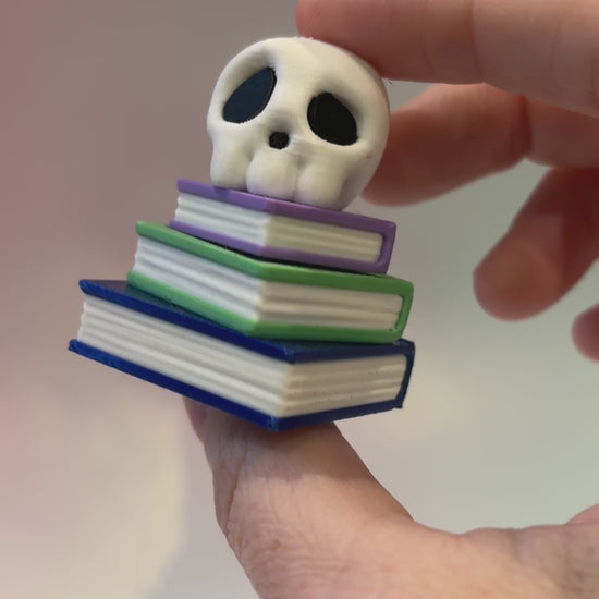 3D printed skull fidget clicker on a colorful stack of books.