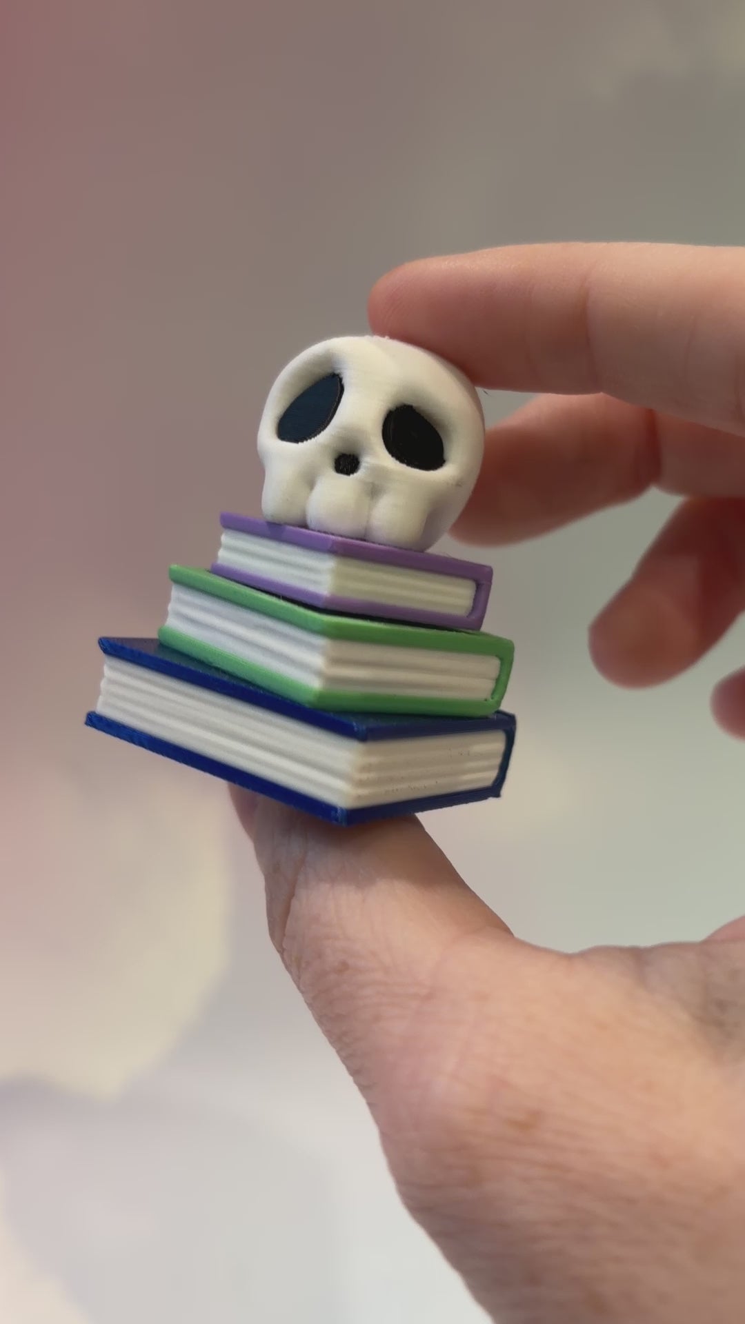 3D printed skull fidget clicker on a colorful stack of books.