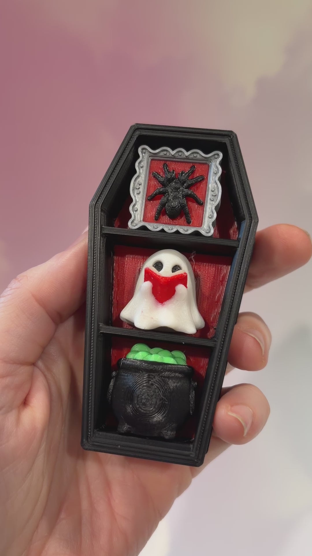 Mini 3D printed black coffin shelf fidget clicker with silver gothic trim and red interior. Features three decorative keycaps: a framed black spider, a ghost reading a book, and a bubbling green cauldron. Includes a silver keychain and is available with clicky or silent switches.