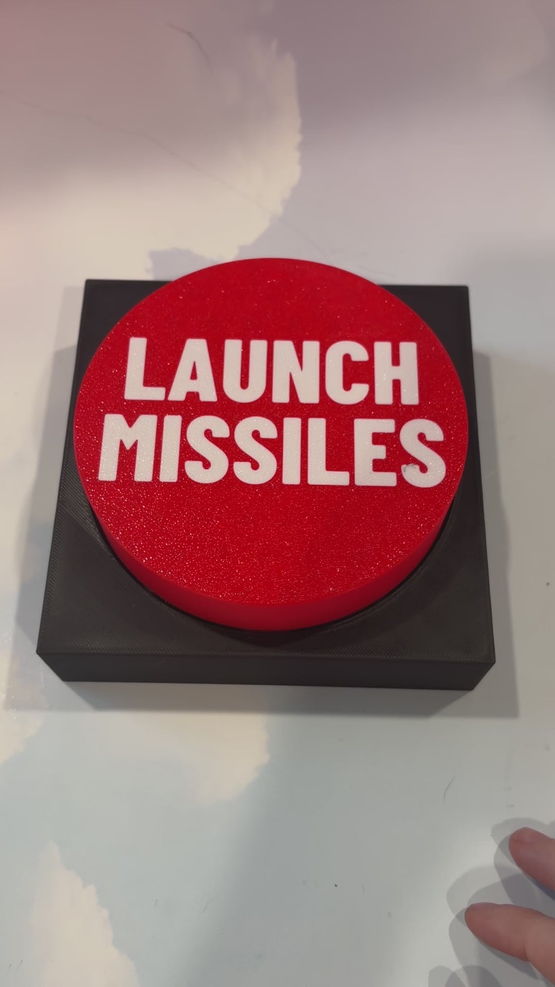 Oversized red 3D printed fidget button with white “LAUNCH MISSILES” lettering on a black square base, shown on a white surface.