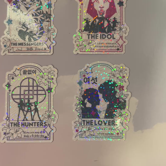 Holographic vinyl tarot sticker set featuring KPOP demon hunter characters: Lovers, Idol, Hunters, and Messengers. Vibrant, 3-inch water-resistant decals. Featuring Huntrix, The Saja Boys, Derpy Tiger, and Rumi and Jinu.