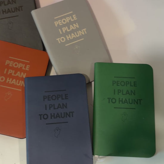 Mini blue notebook with “People I Plan to Haunt” laser engraved in black lettering and a tiny ghost illustration. Approximately 4 x 2.5 inches, with 50 lined pages. Available in brown, green, blue, gray, and black.
